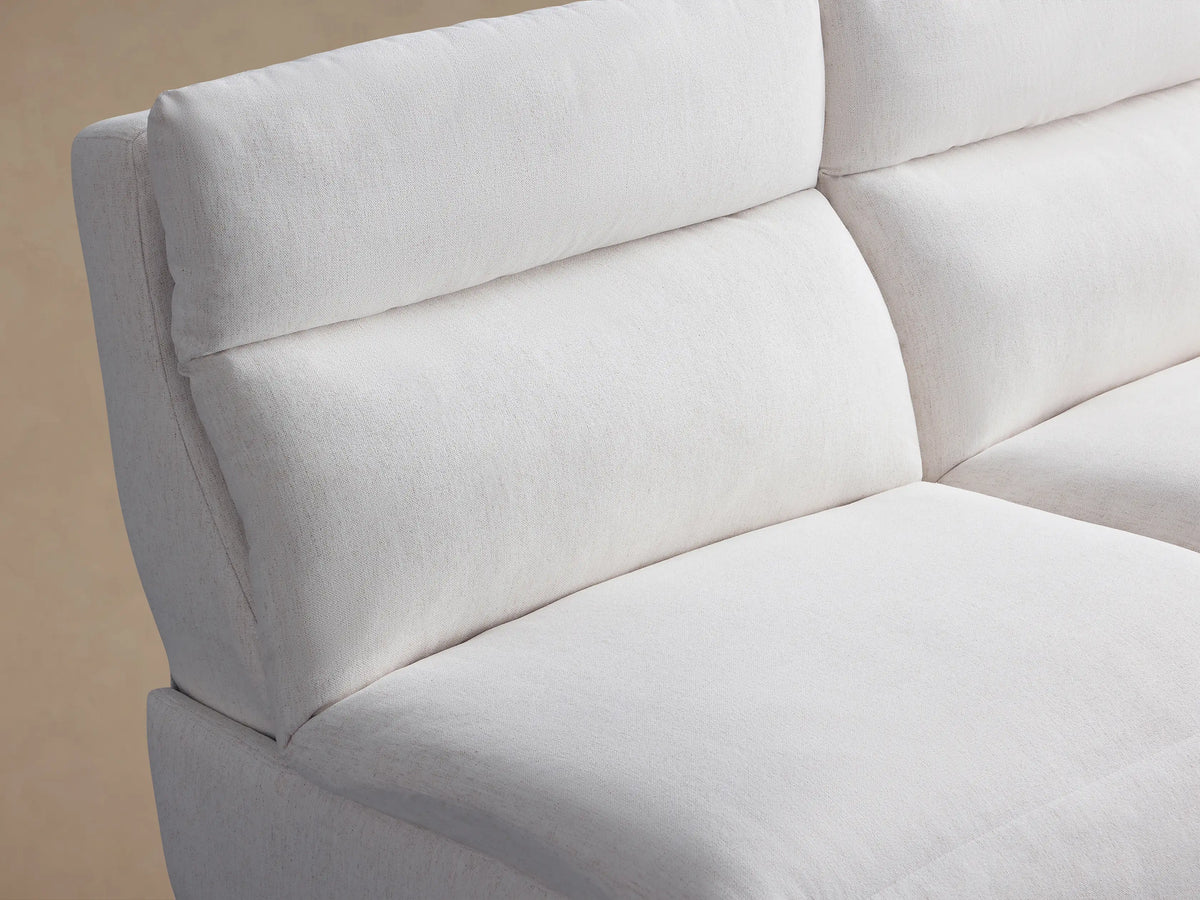 White Rowland Tailored Four-Piece Armless Modular Sofa, with four plush sections, against a beige wall on a wood floor.