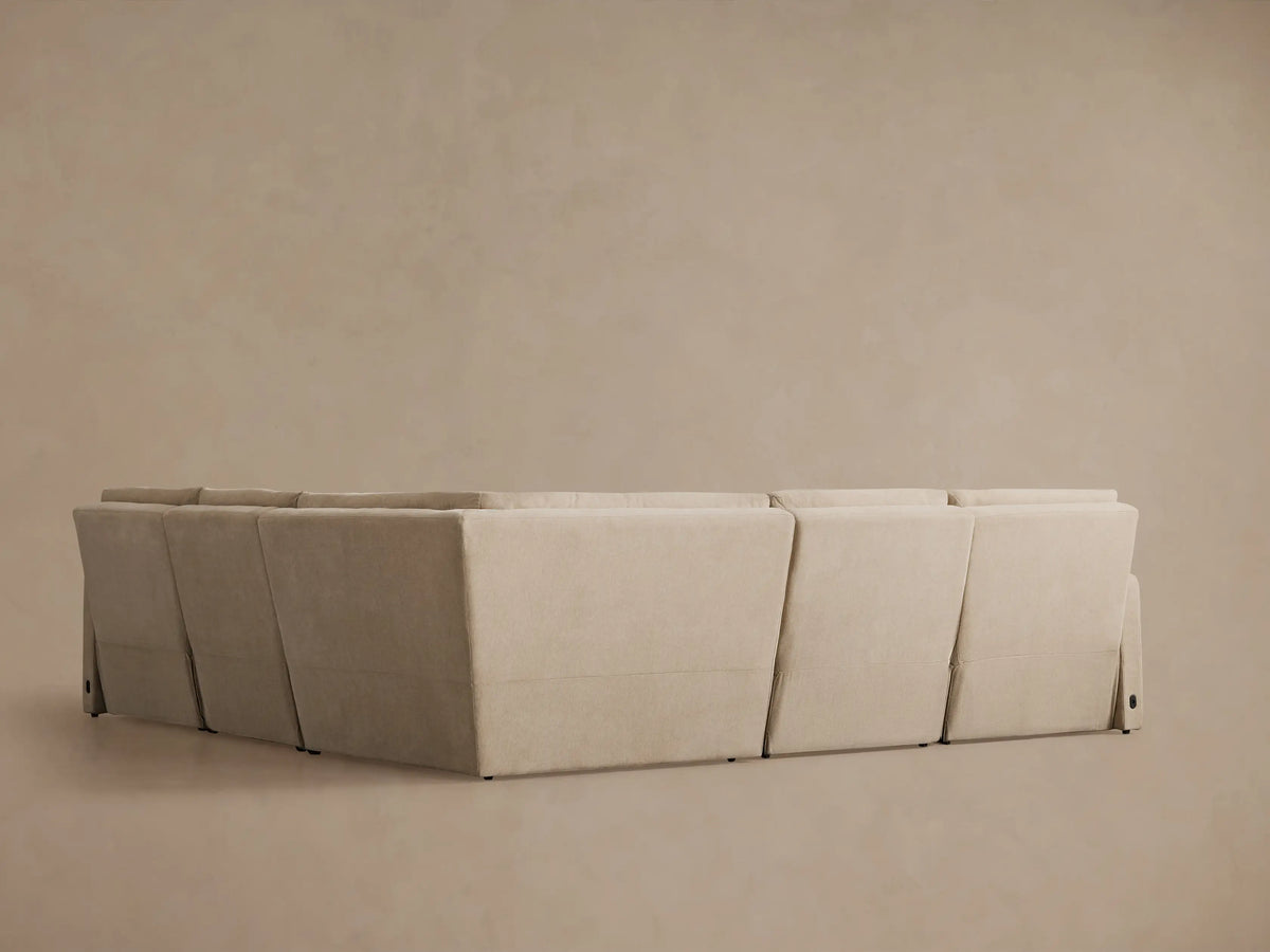 Rowland Tailored Five-Piece Motion Corner Sectional in light beige, L-shaped, with one recliner extended, against a warm taupe wall.