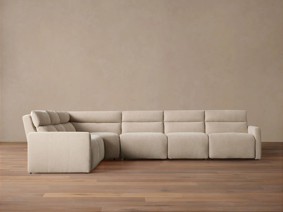 Rowland Tailored Six-Piece Motion Sectional, light beige fabric, L-shaped, on a hardwood floor against a muted tan wall.