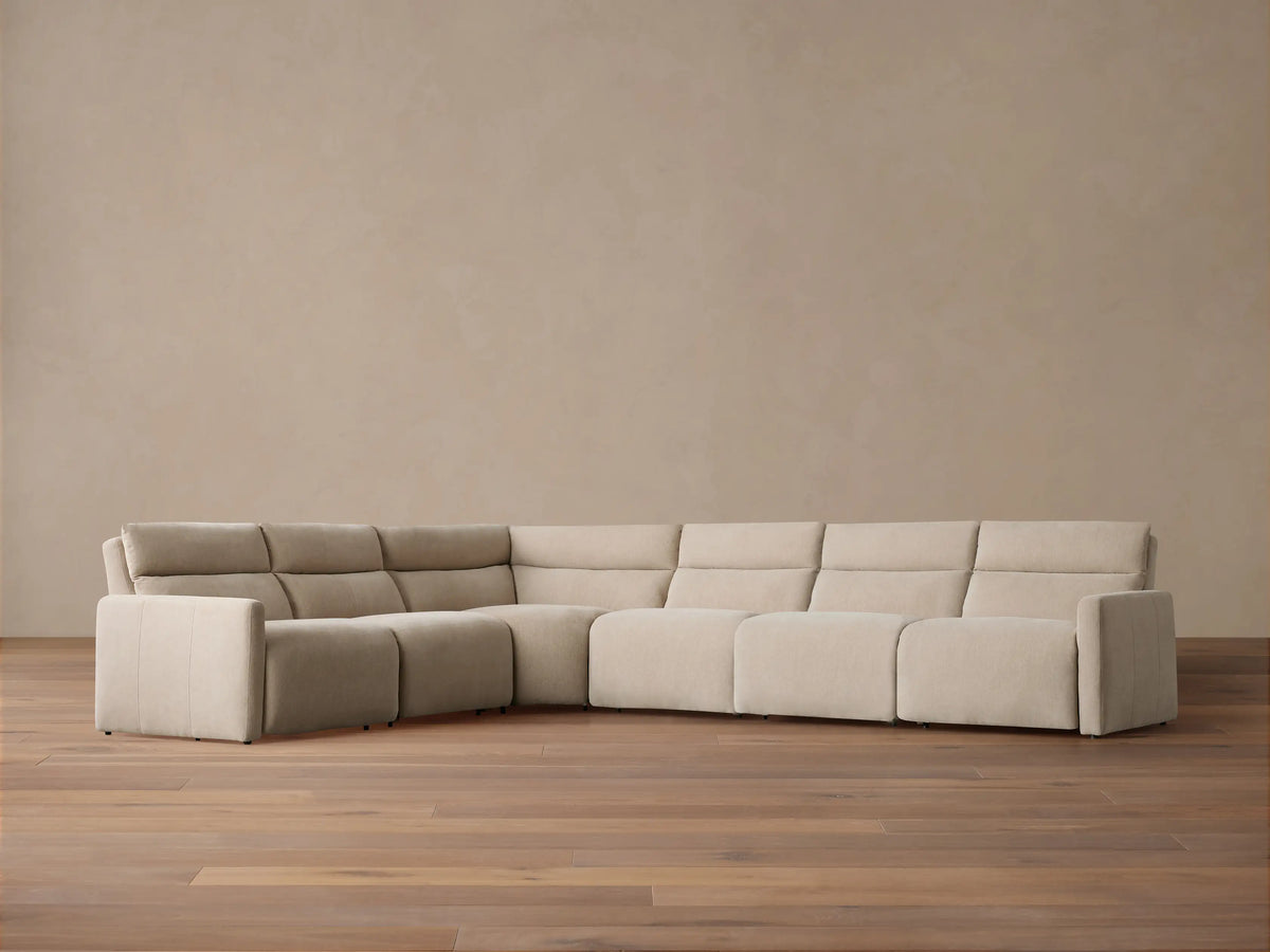 Rowland Tailored Six-Piece Motion Sectional, light beige fabric, L-shaped, on a hardwood floor against a muted tan wall.