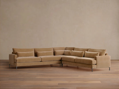 Sumner Three-Piece Corner Sectional in light brown fabric, featuring plush cushions and lumbar pillows, set on wood flooring.