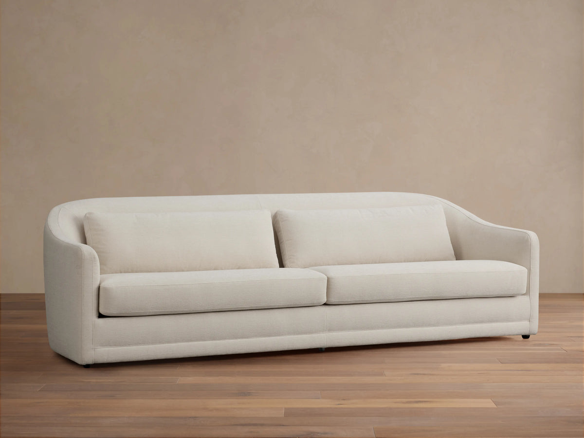 Front view of the cream Bianca Sofa with three decorative throw pillows, in a traditional living room with a brown armchair.