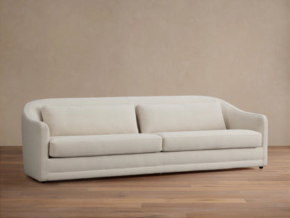Front view of the cream Bianca Sofa with three decorative throw pillows, in a traditional living room with a brown armchair.