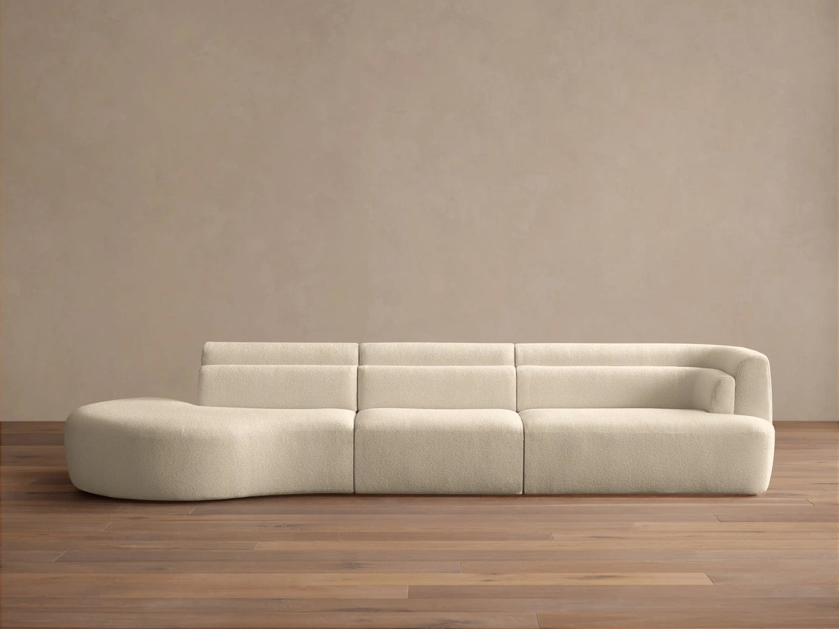 Lovina Three-Piece Bumper Sectional in cream textured fabric, with a rounded chaise left and armrest right, on a wooden floor.