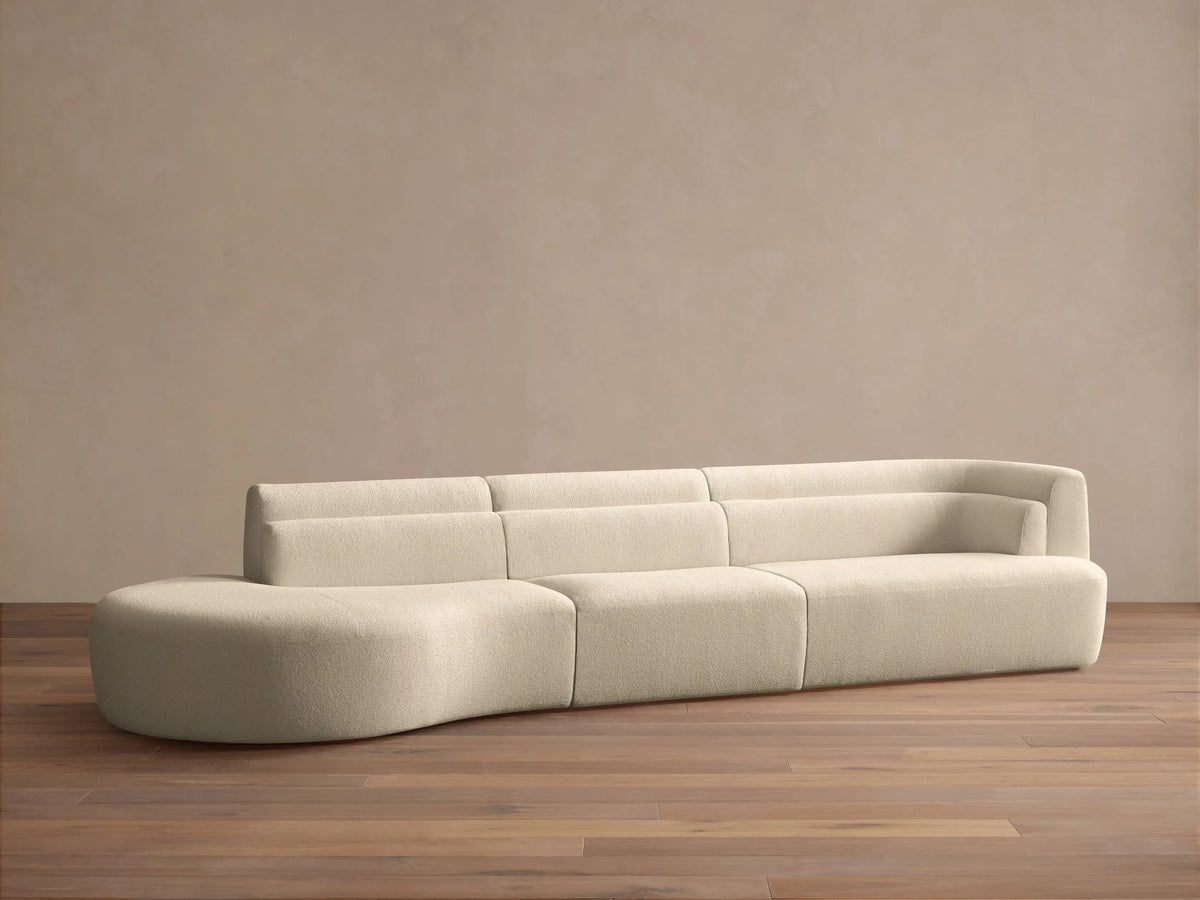 Lovina Three-Piece Bumper Sectional in cream textured fabric, with a rounded chaise left and armrest right, on a wooden floor.