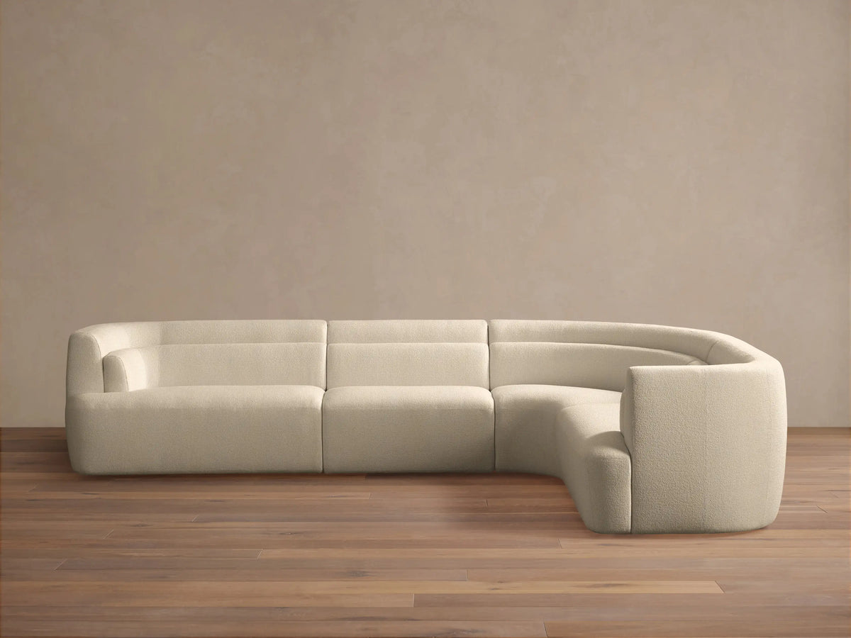Lovina Four-Piece Sectional: L-shaped sofa in cream textured fabric, with a curved corner, on wood floor, light wall.