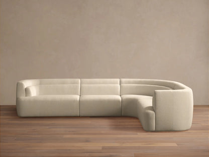Lovina Four-Piece Sectional: L-shaped sofa in cream textured fabric, with a curved corner, on wood floor, light wall.