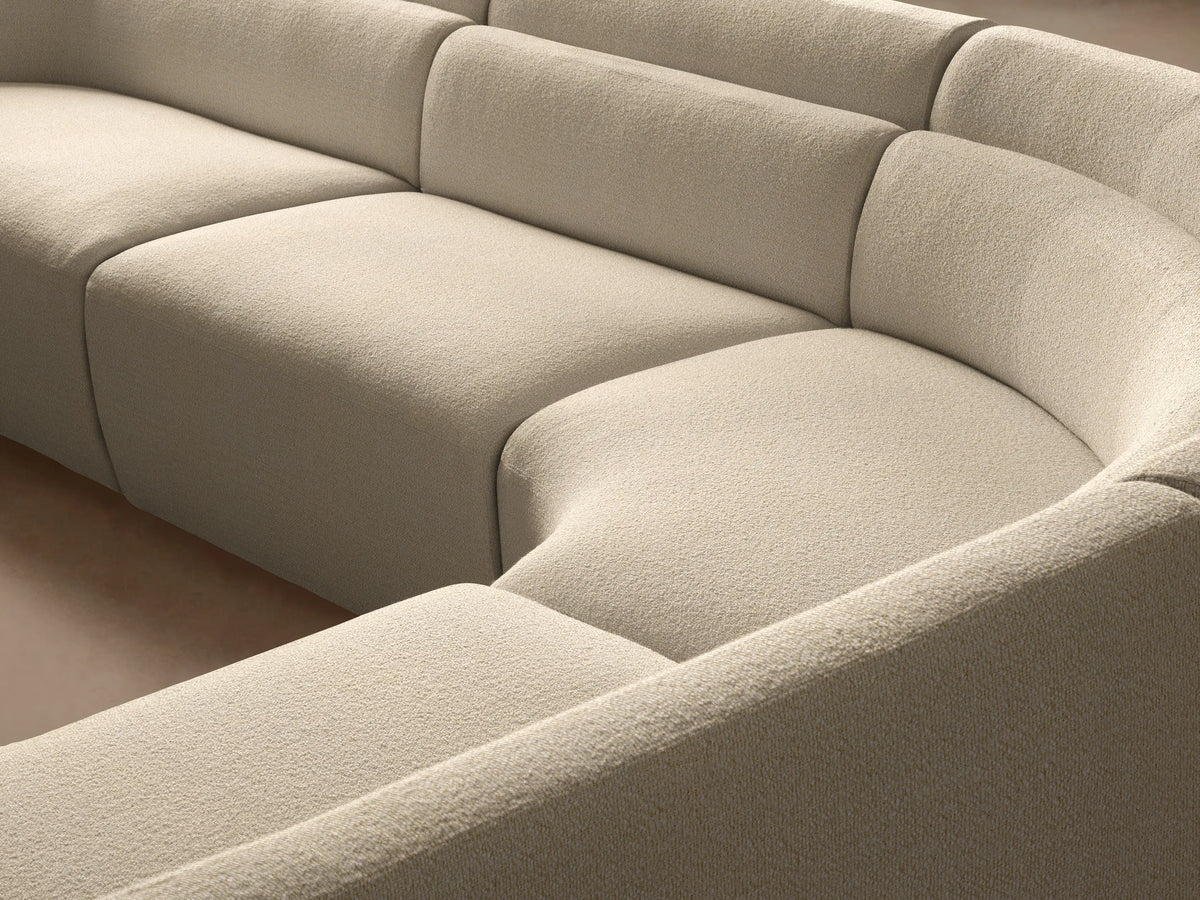Lovina Four-Piece Sectional, curved, upholstered in cream-colored, textured fabric on a wooden floor in a modern room.