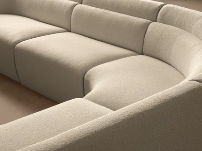 Lovina Four-Piece Sectional, curved, upholstered in cream-colored, textured fabric on a wooden floor in a modern room.