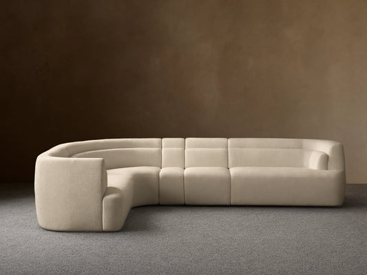 Lovina Four-Piece Sectional: L-shaped sofa in cream textured fabric, with a curved corner, on wood floor, light wall.