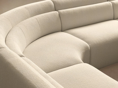 Lovina Five-Piece Sectional with Ottoman, light beige, curved, on a wooden floor against a tan wall.