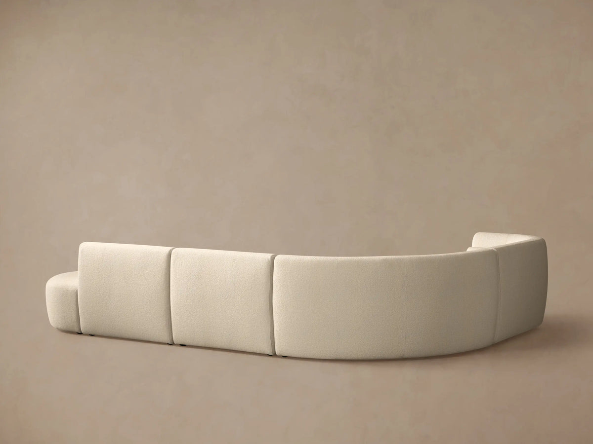 Close-up, angled view of a light cream Lovina Five-Piece Sectional, showing its curved design and textured fabric.
