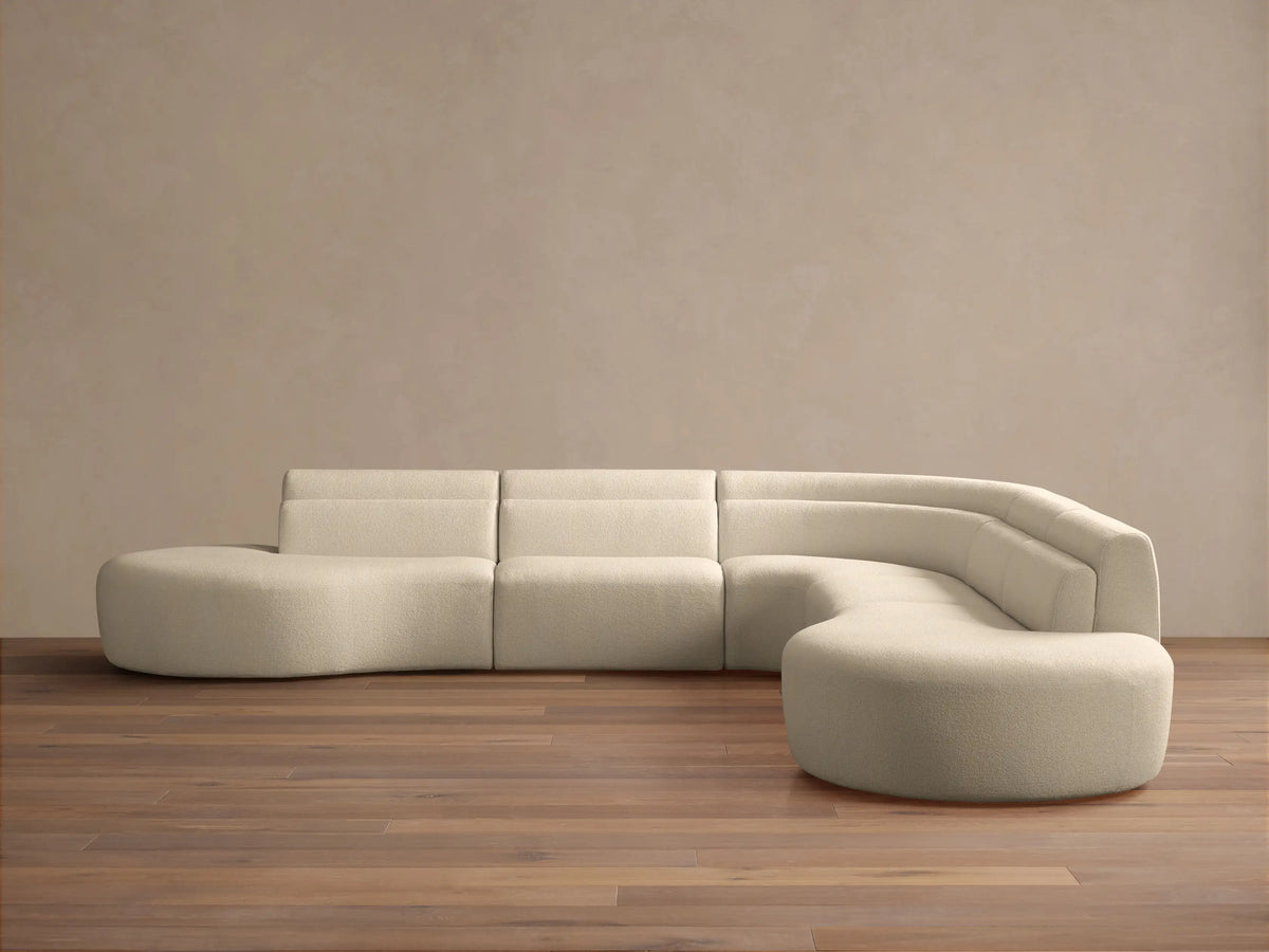 Cream bouclé Lovina Five-Piece Corner Sectional, L-shaped with curved right end, on wood floor against a neutral wall.