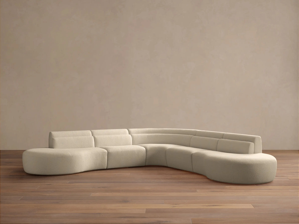 Cream bouclé Lovina Five-Piece Corner Sectional, L-shaped with curved right end, on wood floor against a neutral wall.