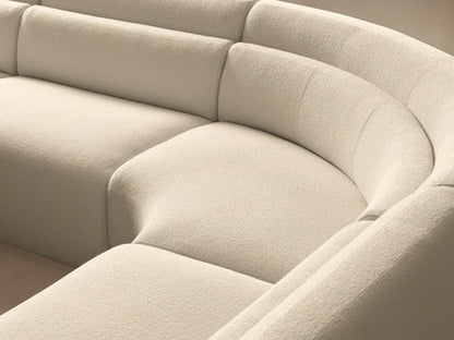Lovina Five-Piece Corner Sectional: A large, curved light beige sofa on a warm wooden floor against a pale wall.