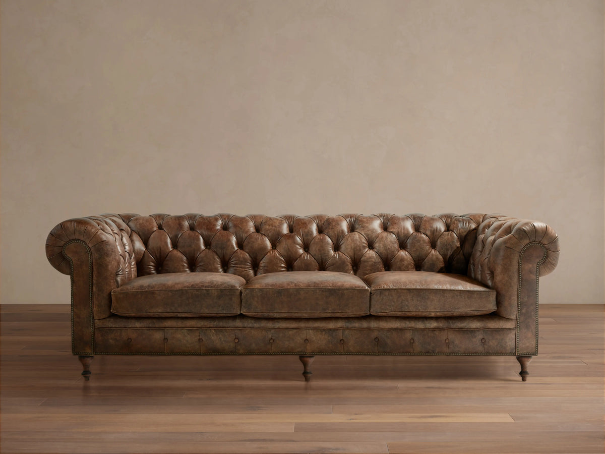 Full-length Wessex Leather Sofa with distressed brown tufted back, rolled arms, three seat cushions, nailhead trim, on wood floor.
