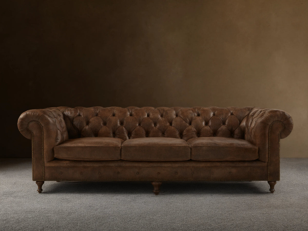 Full-length Wessex Leather Sofa with distressed brown tufted back, rolled arms, three seat cushions, nailhead trim, on wood floor.