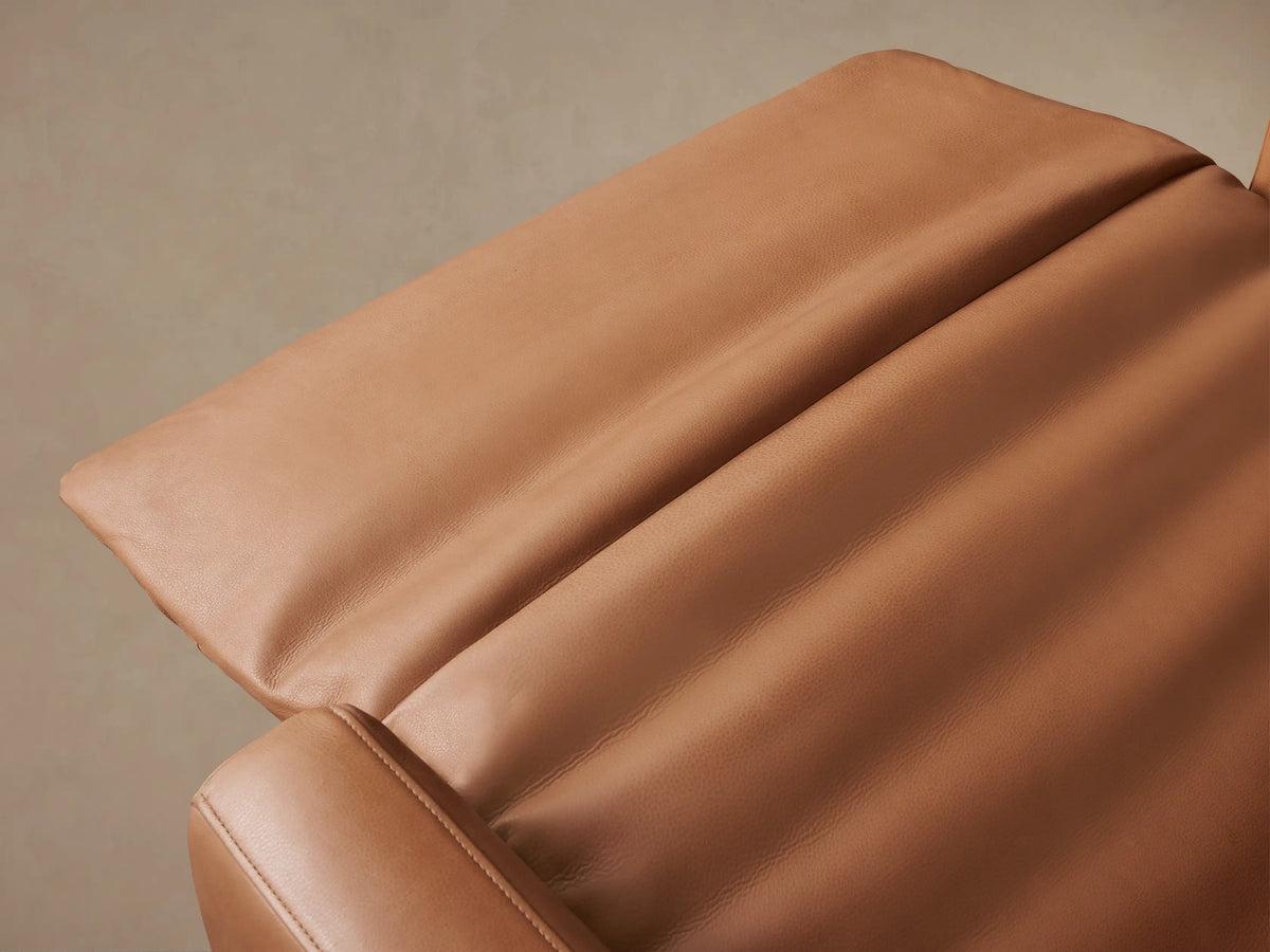 Front view of the Rowland Tailored High-Back Motion Recliner, upholstered in rich caramel leather, standing upright on a wood floor.