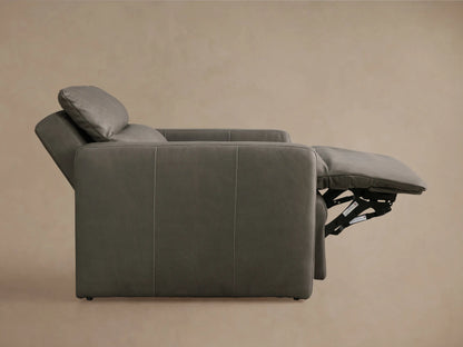 Charcoal gray Rowland Tailored Leather High-Back Motion Recliner, angled view, footrest extended, against a light brown wall.