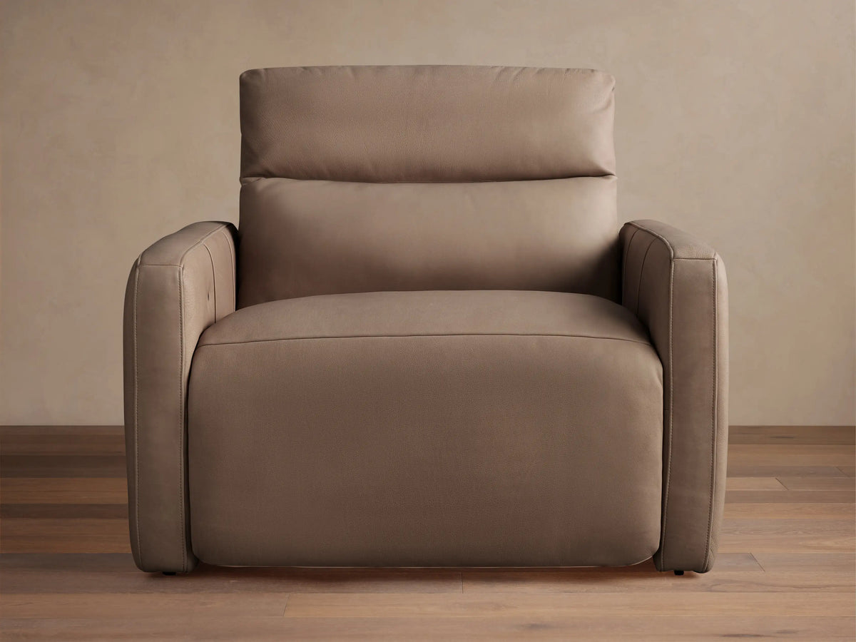 Taupe Rowland Tailored Leather High-Back Motion Recliner with visible stitching, standing on a hardwood floor against a light wall.