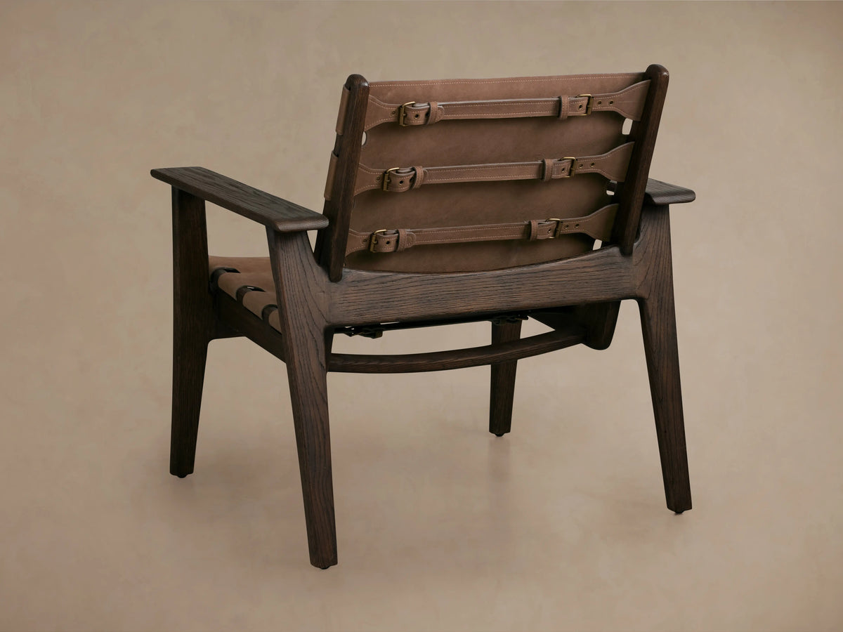 Reggie Nubuck Leather Chair backrest with brown leather sling-style, secured by antique brass buckles, oak wood frame visible.