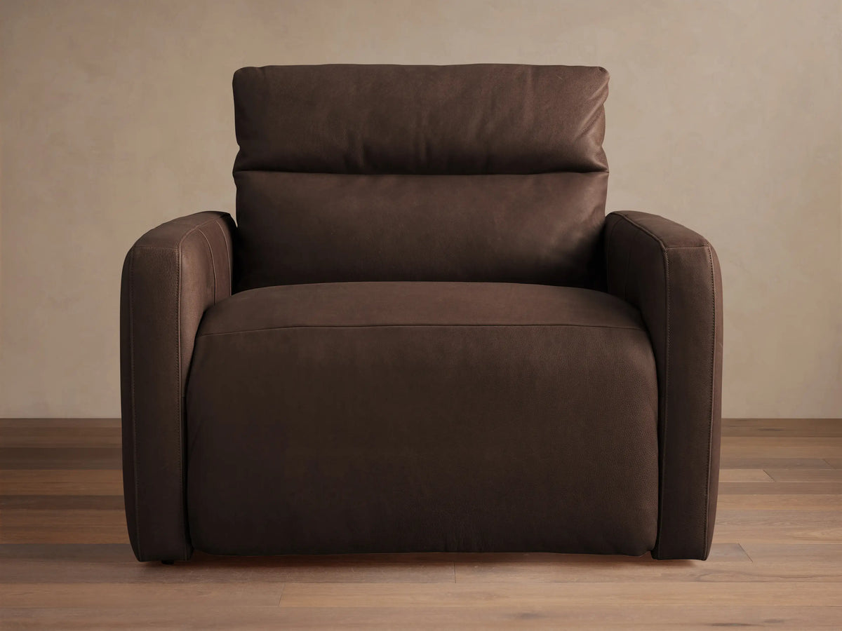 Rowland Tailored dark brown leather high-back motion recliner. Angled view, tailored design, plump cushions, on wood floor.