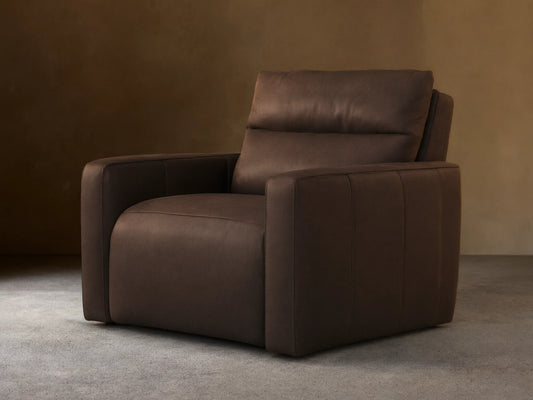 Rowland Tailored dark brown leather high-back motion recliner. Angled view, tailored design, plump cushions, on wood floor.