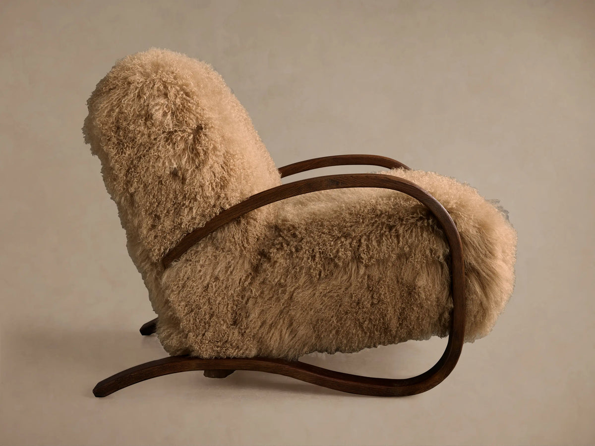 Allora Mongolian Shearling Chair close-up. Plush cream shearling texture with a curved dark mocha wood armrest.