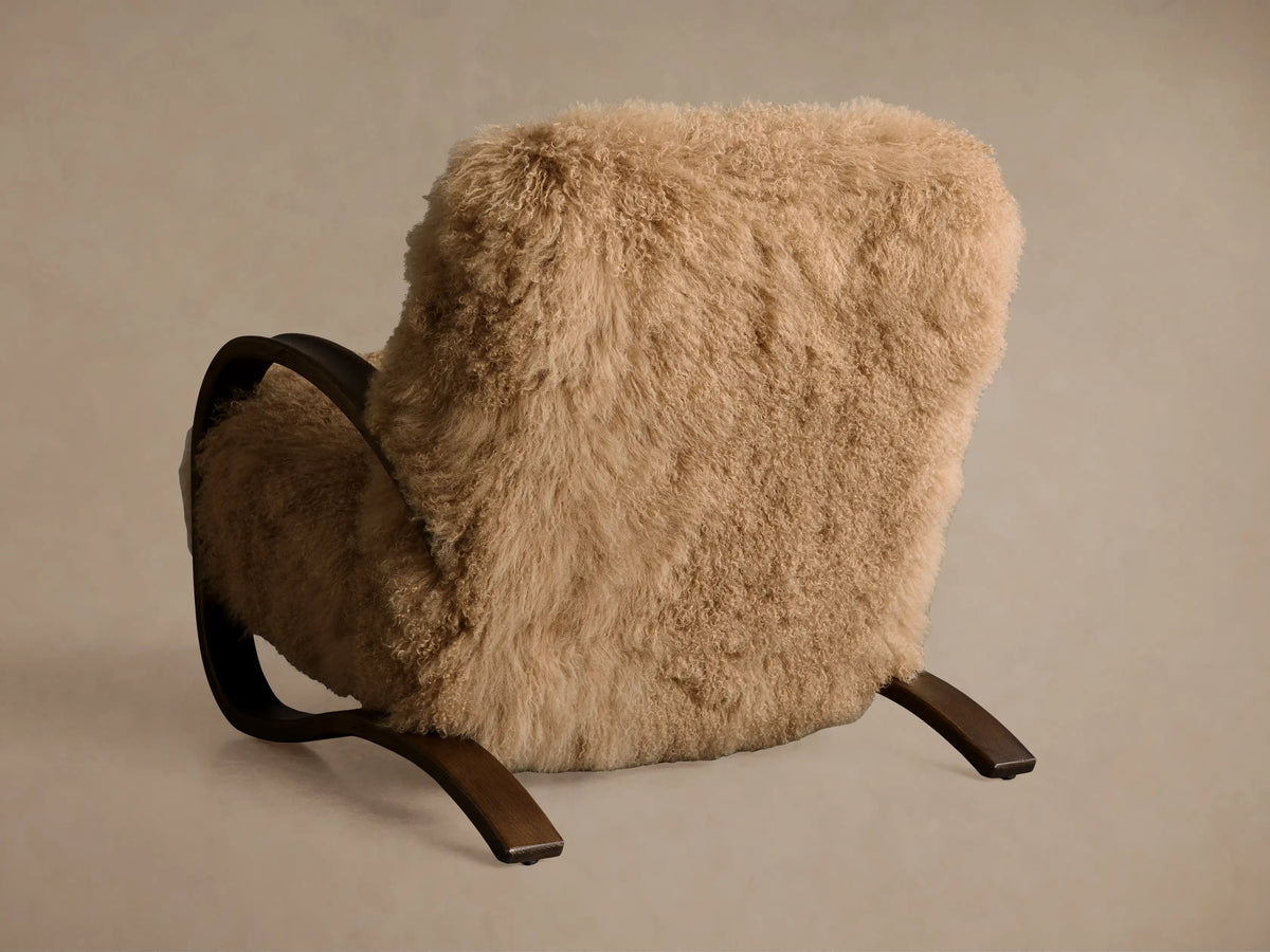Allora Mongolian Shearling Chair, angled, with curly light beige shearling and dark curved wood frame against a neutral background.