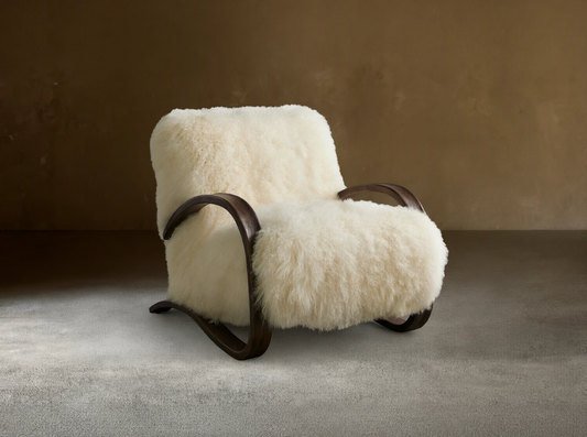 Allora Mongolian Shearling Chair. Creamy white fluffy shearling armchair with dark curved wood frame on a wooden floor.