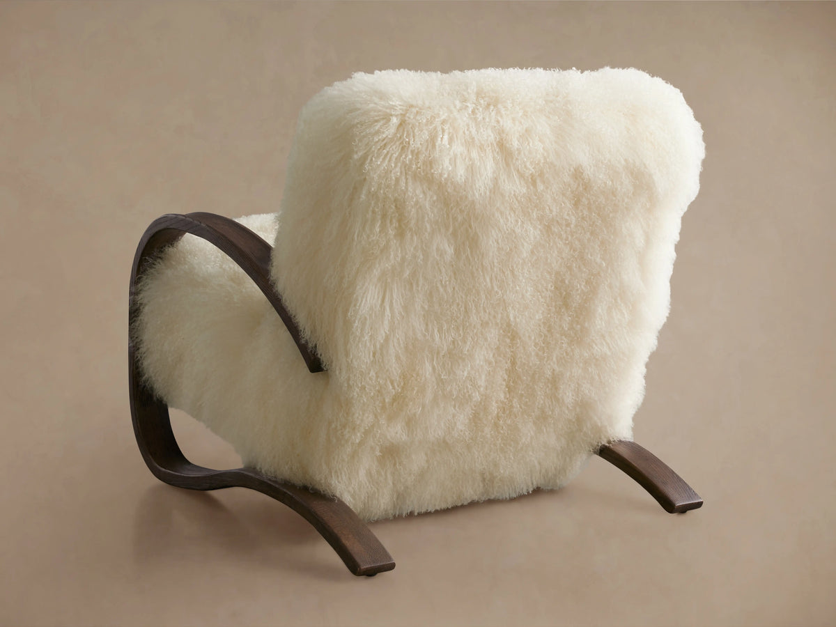Allora Mongolian Shearling Chair: Close-up of a cozy cream shearling chair with curved dark mocha wood arms and base frame.