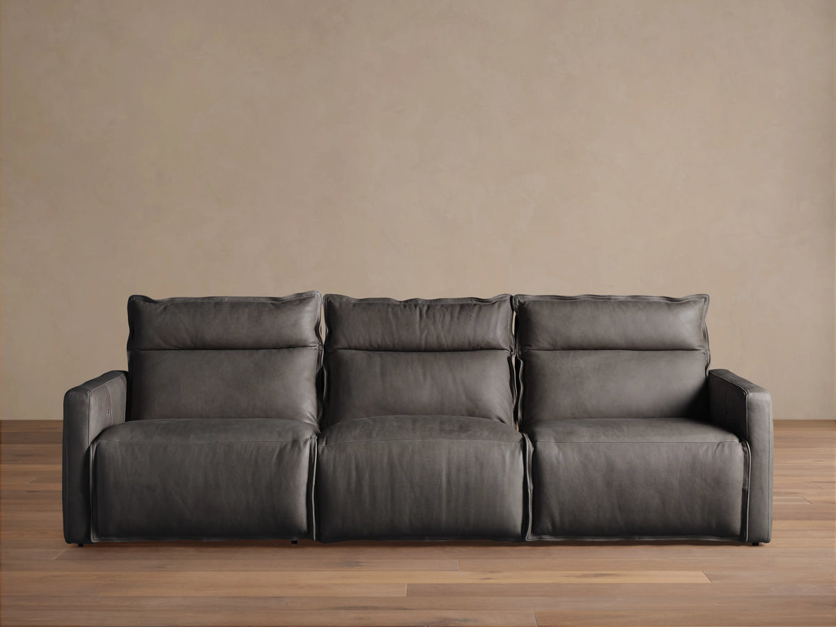 A three-piece Rowland Leather Motion Modular Sofa, in dark leather, with left, armless, and right recliners, on a wooden floor.