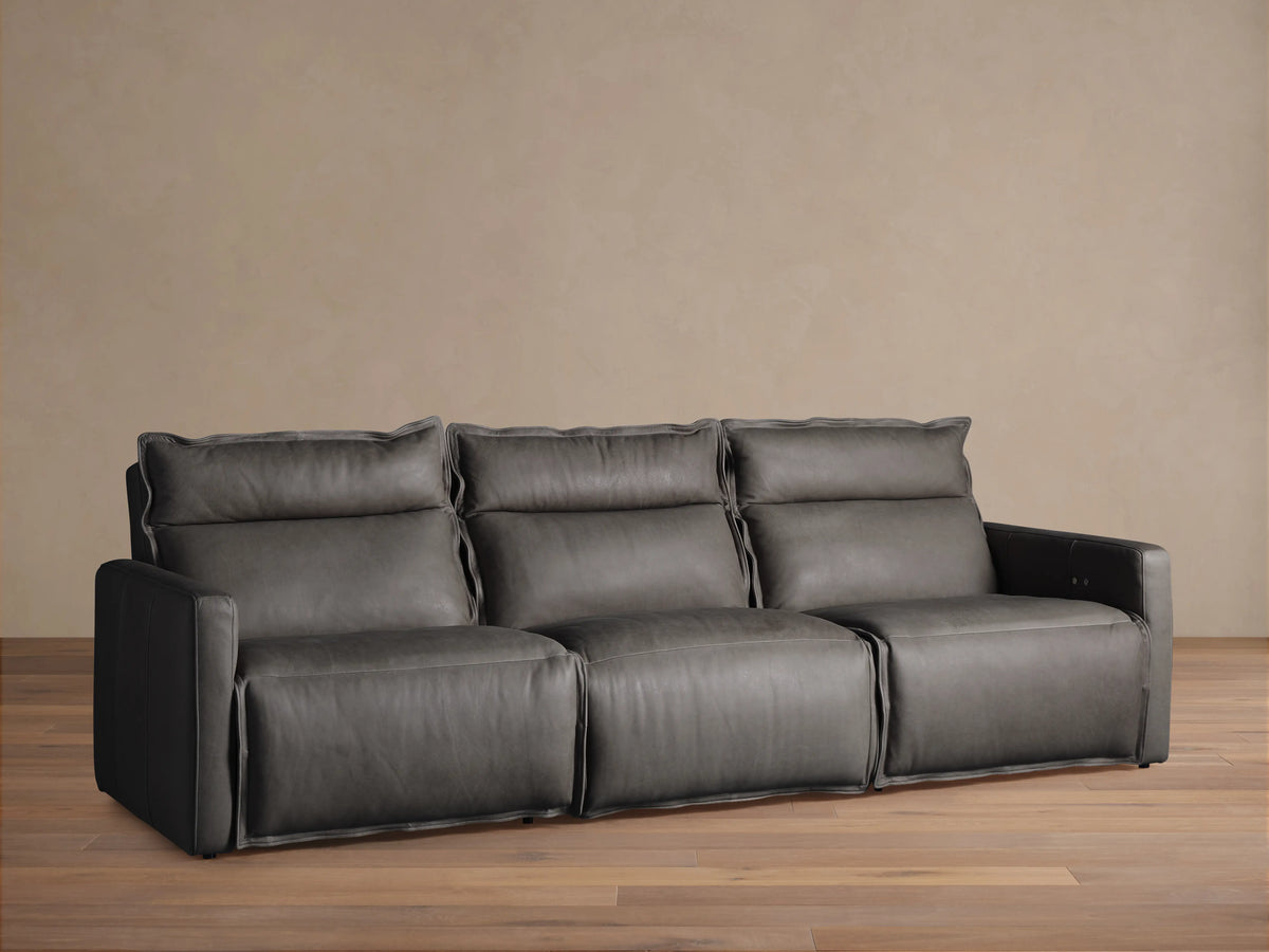 A three-piece Rowland Leather Motion Modular Sofa, in dark leather, with left, armless, and right recliners, on a wooden floor.