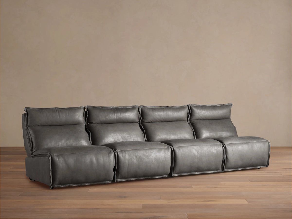 Rowland Leather Four-Piece Armless Motion Modular Sofa in dark gray leather, featuring four connected recliners on a wooden floor against a beige wall.