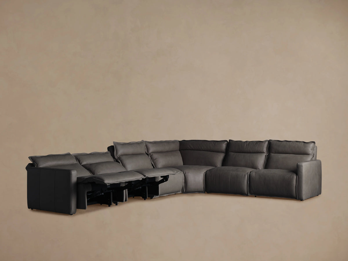 Alt text: Rowland Leather Six-Piece Motion Sectional in dark gray. The sectional is viewed from the back, showing its L-shape and smooth leather finish.