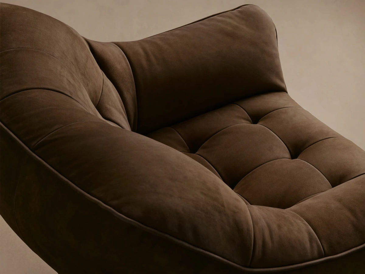 Front view of a brown distressed leather armchair with a tufted back, rounded arms, and a dark wood base with an X-shaped crossbar.