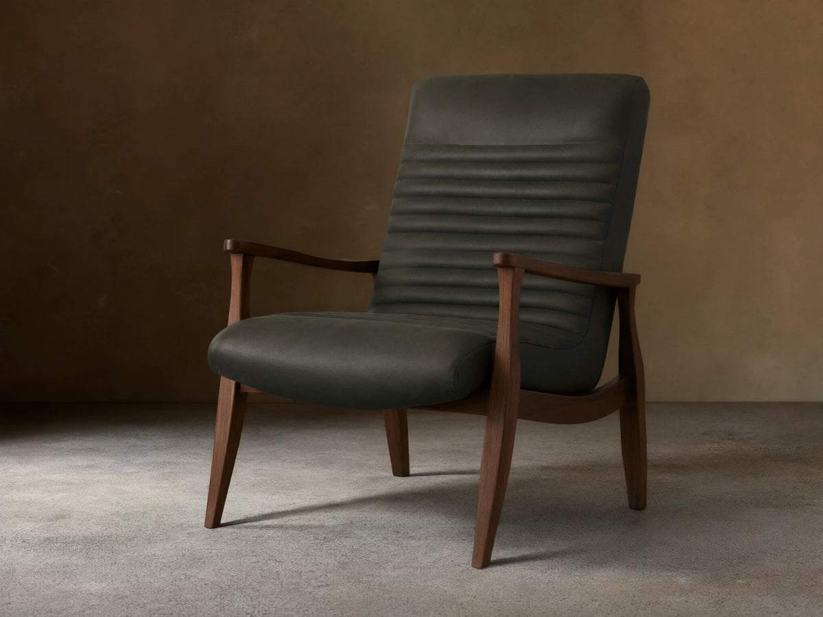 Nathaniel Leather Chair with dark leather upholstery, horizontal stitching on backrest, and wooden arms and legs on a wood floor.