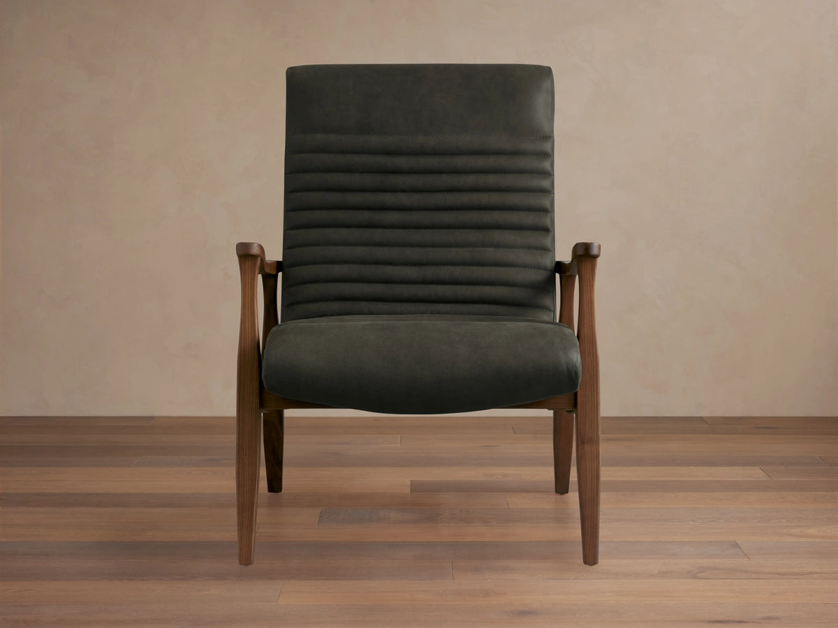 Nathaniel Leather Chair with dark leather upholstery, horizontal stitching on backrest, and wooden arms and legs on a wood floor.