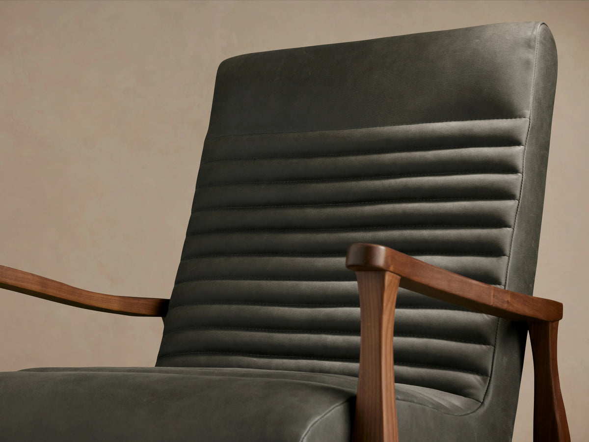 Nathaniel Leather Chair in dark leather with ribbed backrest, wooden arms and legs, on a wooden floor, front view.