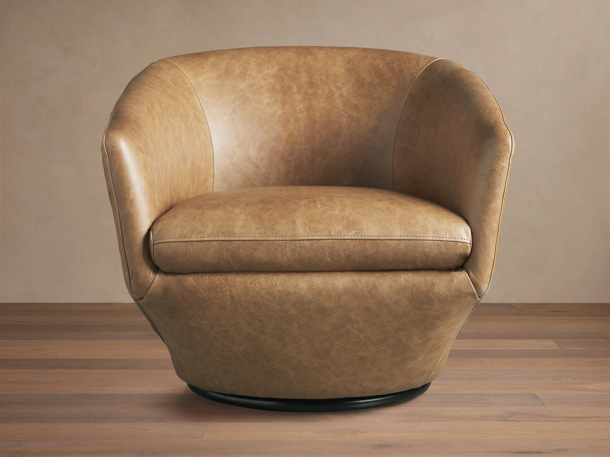 Pelton Leather Swivel Chair. Distressed tan leather barrel armchair with visible stitching, a plump seat, and a black swivel base.