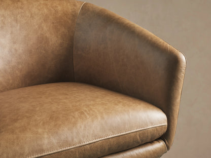Close-up of the Pelton Leather Swivel Chair, showing a warm, distressed brown leather seat and curved armrest with fine stitching.