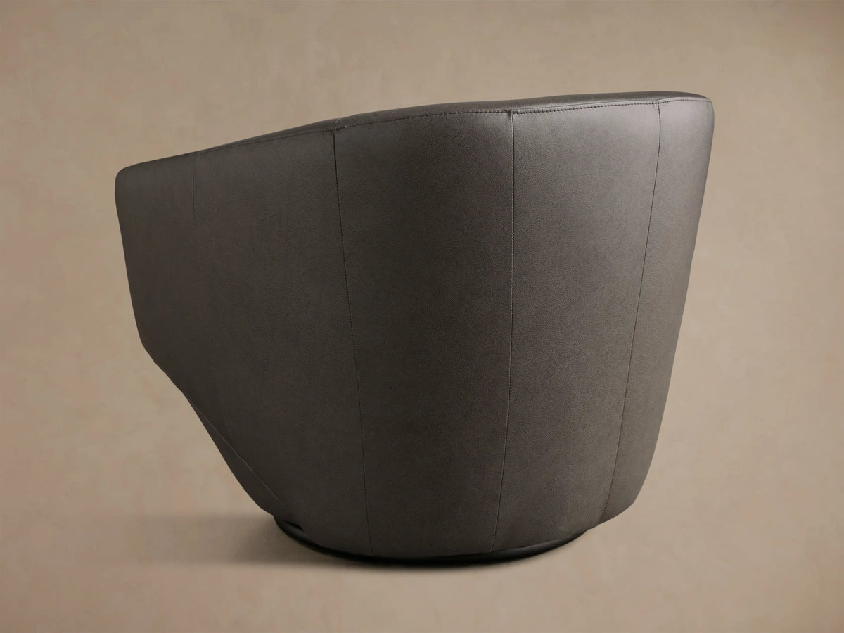 Side profile of a dark gray Pelton Leather Swivel Chair, highlighting its smooth, curved design and armrest.