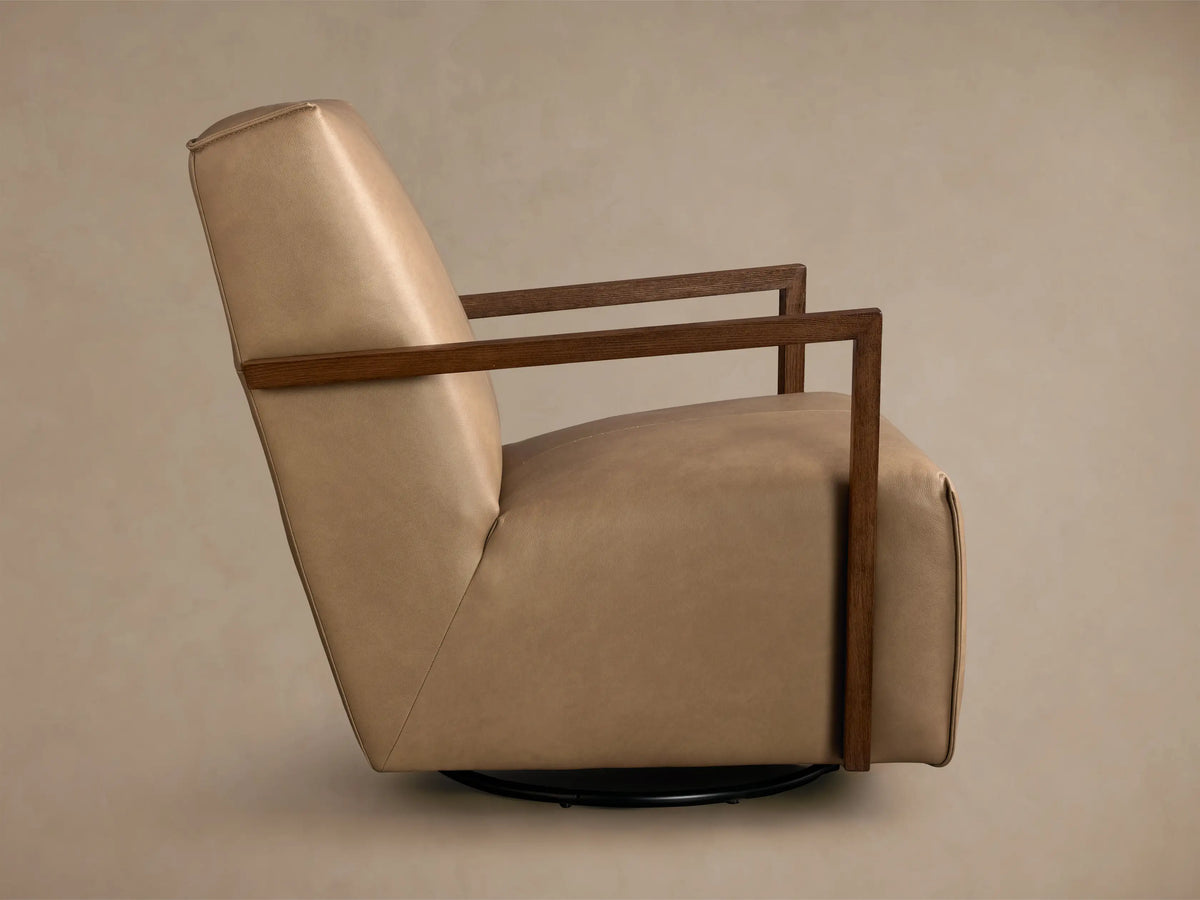 Rear view of the tan Walsh Leather Swivel Glider, featuring stitched leather upholstery, dark wood armrests, and a black swivel base.