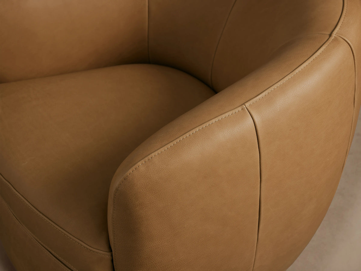 Cerrito Leather Swivel Chair in tan leather, featuring a curved backrest and seat, with a solid steel swivel base on a wooden floor.