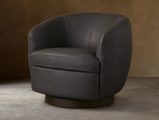 Dark grey Cerrito Leather Swivel Chair with curved back and padded seat cushion on a wooden swivel base, set on a wooden floor.