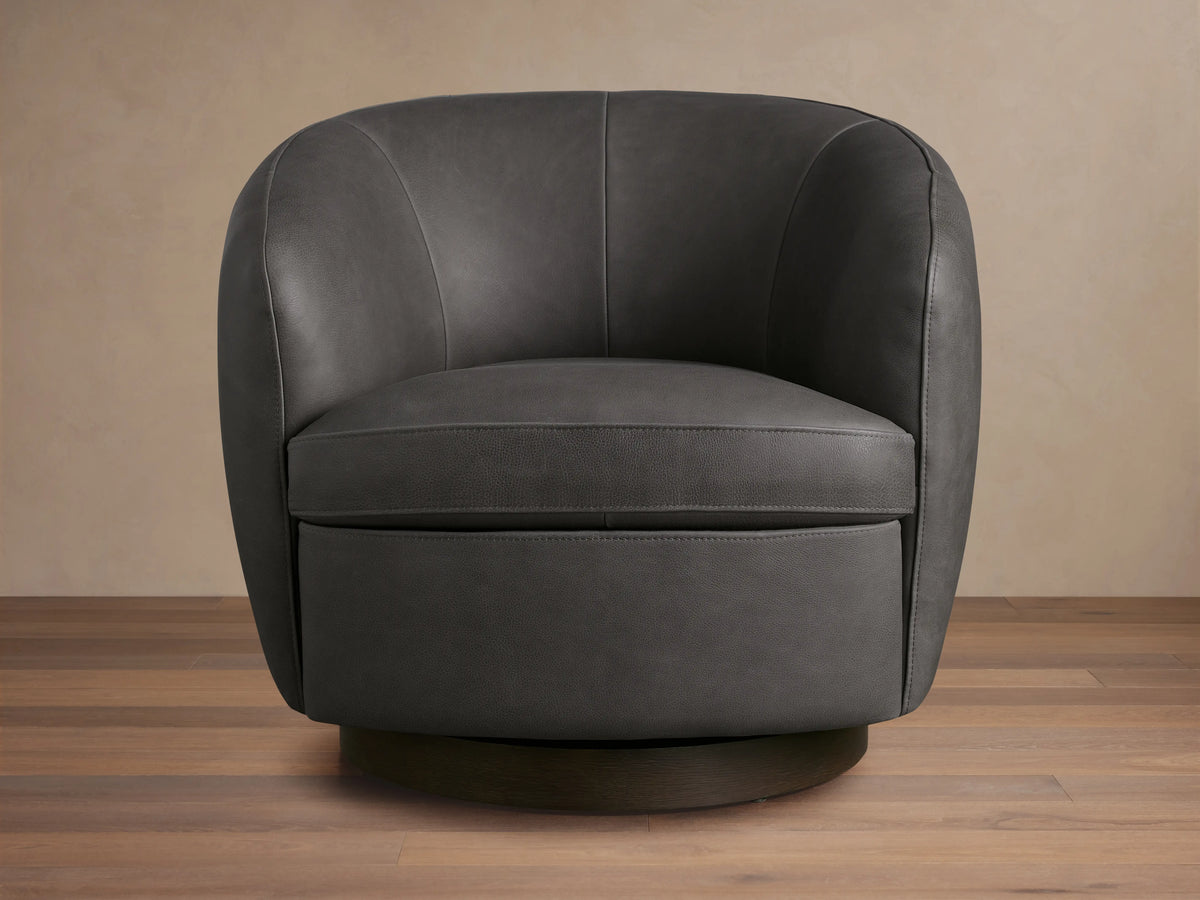 Dark grey Cerrito Leather Swivel Chair with curved back and padded seat cushion on a wooden swivel base, set on a wooden floor.