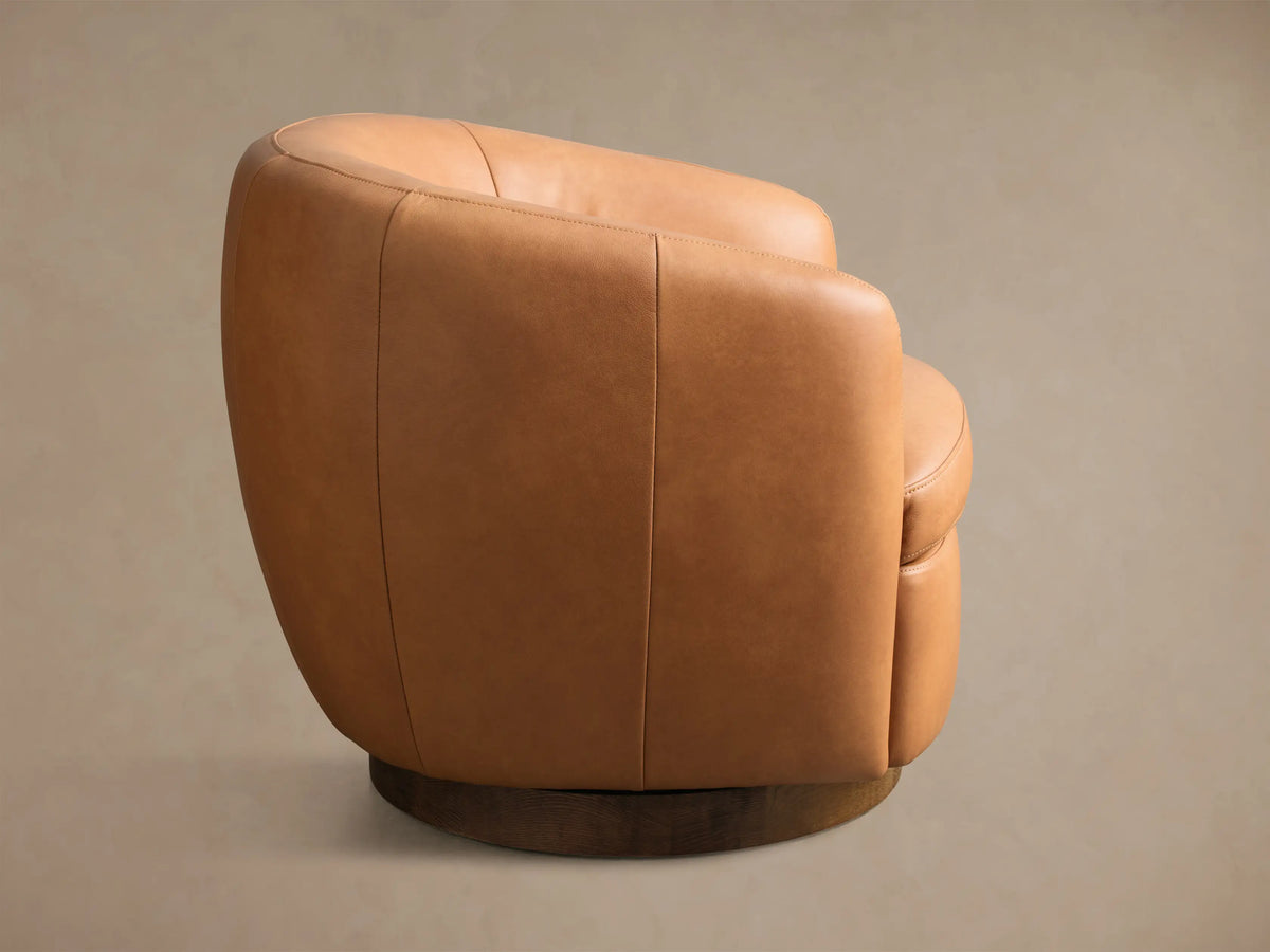 Side view of a tan Cerrito Leather Swivel Chair, showcasing its smooth leather upholstery and dark wooden swivel base.