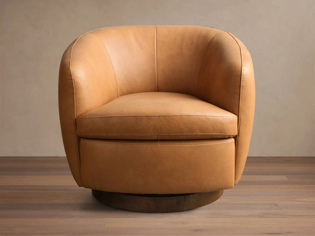 Rear view of the tan Cerrito Leather Swivel Chair, showing its rounded back with vertical stitching and dark wooden swivel base.