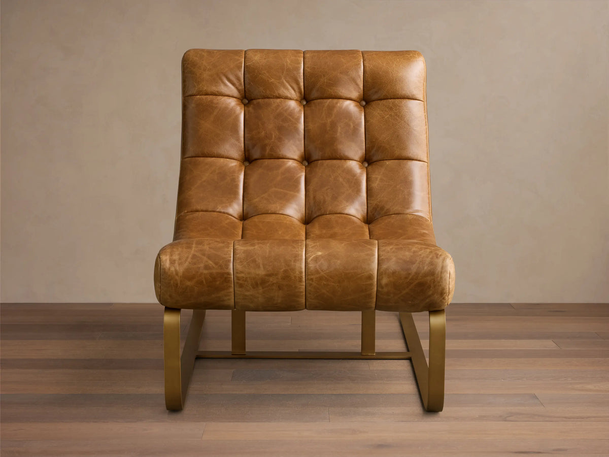 Angled front view of the brown tufted Callaway Leather Chair with a dark frame, next to a beige sectional sofa in a living room.