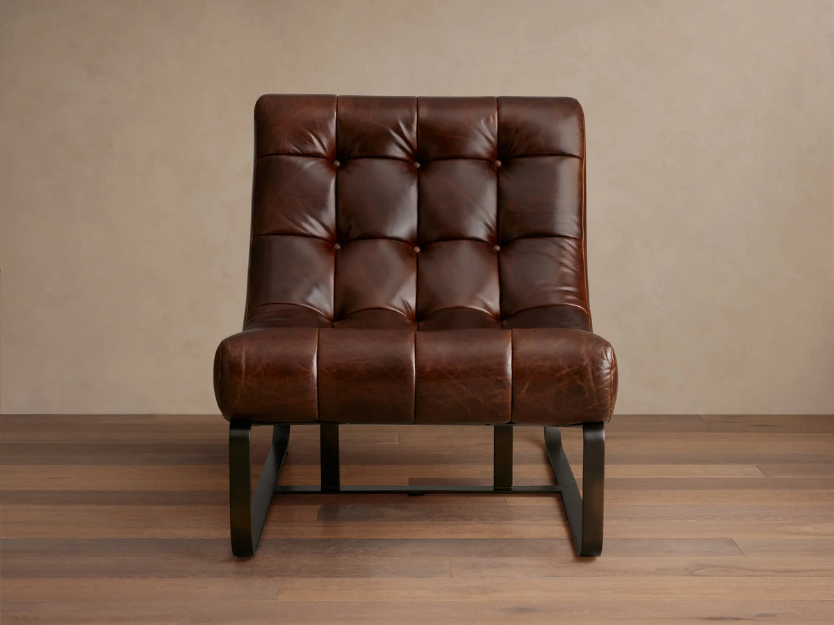 Front-right view of the brown Callaway Leather Chair with a tufted seat and black metal frame in a living room.